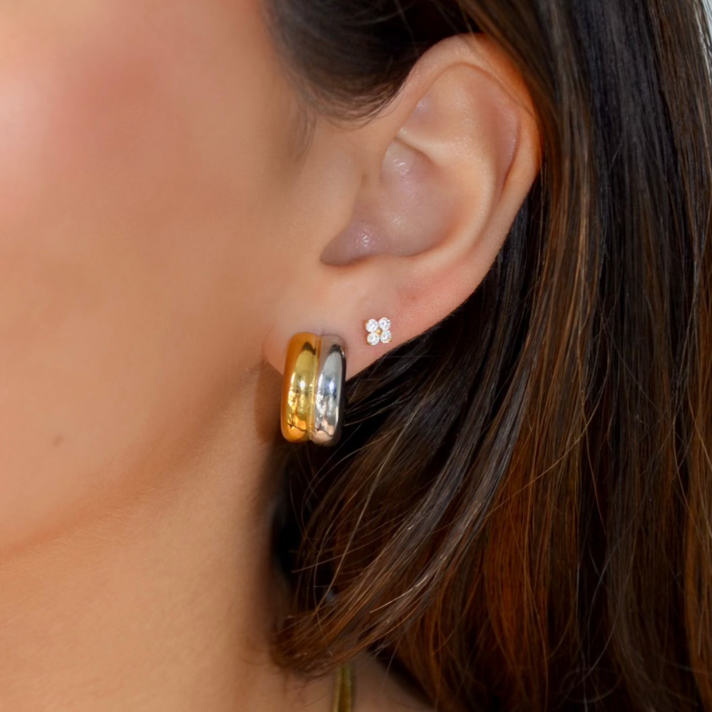 Close-up image of a person’s ear adorned with three sleek, mixed metal hoop earrings from the jewelry brand Azzaik. The earrings are made of stainless steel, ensuring they are hypoallergenic, waterproof, and tarnish-free. The smallest hoop is silver-toned, the middle one is gold-toned, and the largest is a blend of both metals, showcasing practicality without compromising on style.