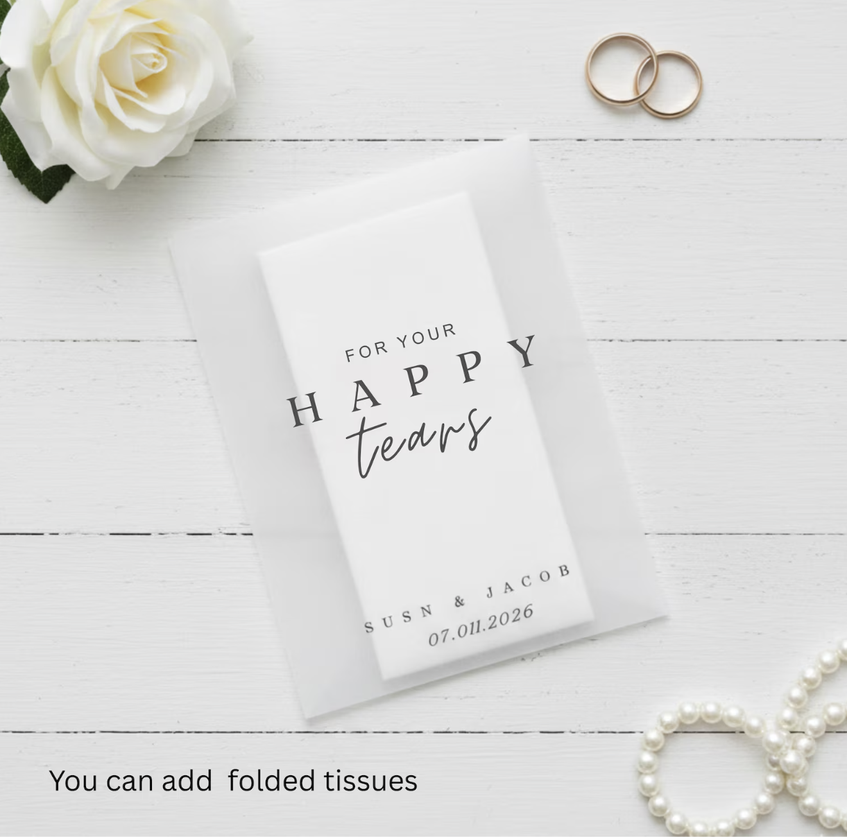 Personalized tissue pack with 'For your happy tears' text on a white wooden surface with flowers and rings.